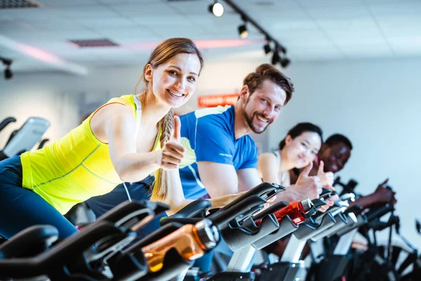 Woman showing thumbs up sign exercising of fitness bike in gym — Stock Photo, Image