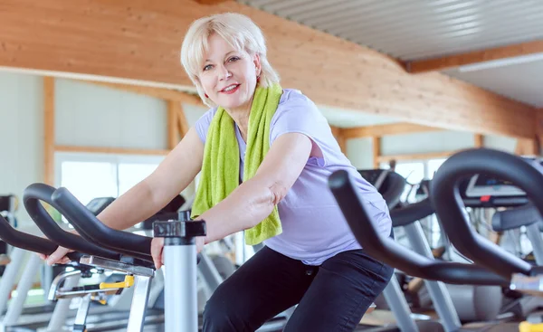 Ανώτερη γυναίκα άσκηση για καλύτερη φυσική κατάσταση σε ένα ποδήλατο στο γυμναστήριο — Φωτογραφία Αρχείου