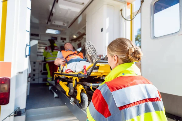 Sağlık görevlileri yaralı adamı ambulansla sedyeye koyuyor. — Stok fotoğraf