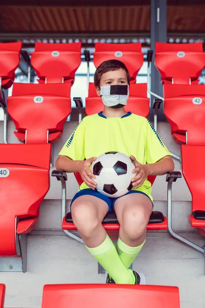 Самотній хлопчик на футбольному стадіоні дивиться гру в масці — стокове фото