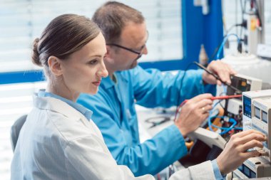 Test bankında iki elektronik mühendisi yeni bir ürünü ölçüyor.