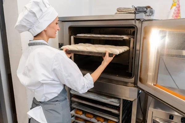 Baker mujer poniendo bandeja para hornear en el horno — Foto de Stock