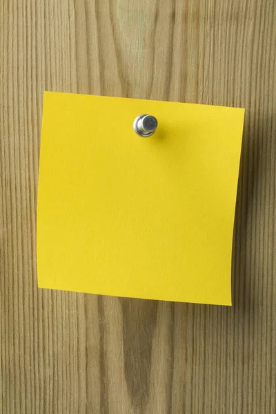 Empty yellow paper post it note pinned to a wooden board