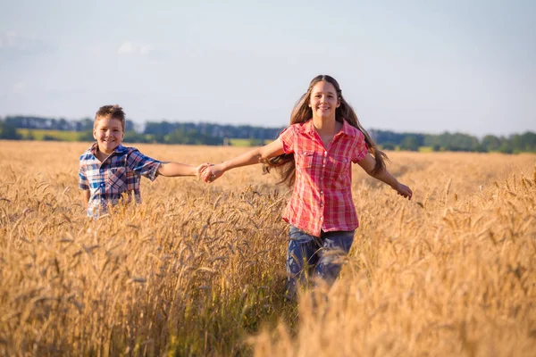 Ragazza e ragazzo in esecuzione sul campo con grano maturo — Foto Stock