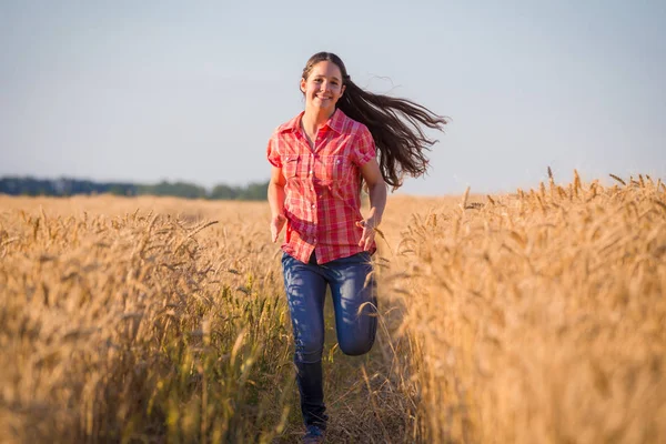 Giovane ragazza che corre sul campo con grano maturo — Foto Stock