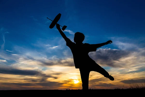 Silhueta de menino com seu avião contra o pôr do sol — Fotografia de Stock