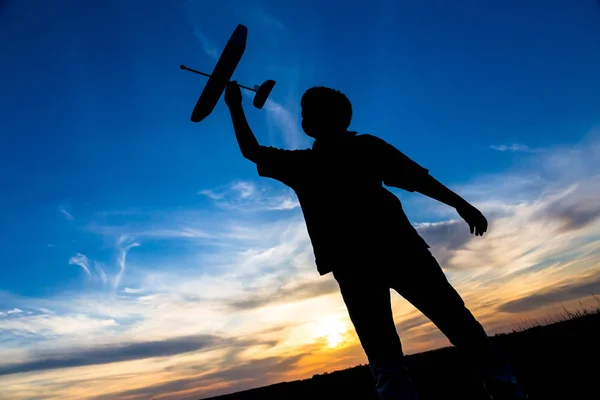 Sylwetka chłopca z jego samolot przeciwko zachód słońca — Zdjęcie stockowe