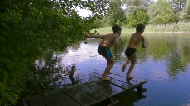 Двоє хлопчиків стрибають до річки з пірсу — стокове відео