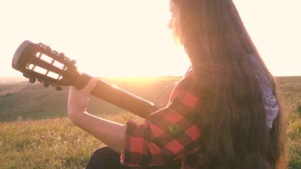 Jovencita tocando la guitarra en el prado al atardecer — Vídeos de Stock