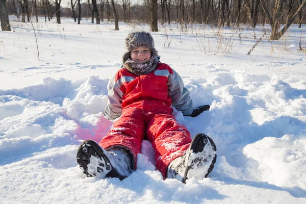 公園で雪に座って微笑む少年 — ストック写真