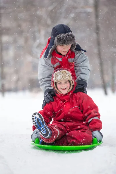 スライドで雪に覆われた公園に乗って二人の幸せな少年 — ストック写真