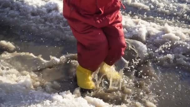 Niño en botas de lluvia saltando en el charco de hielo, cámara lenta — Vídeos de Stock