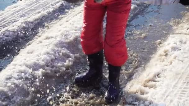 Niño en botas de lluvia saltando en el charco de hielo, cámara lenta — Vídeo de stock