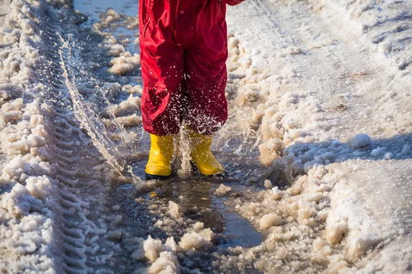 Miúdo de botas de chuva a saltar para a poça de gelo — Fotografia de Stock