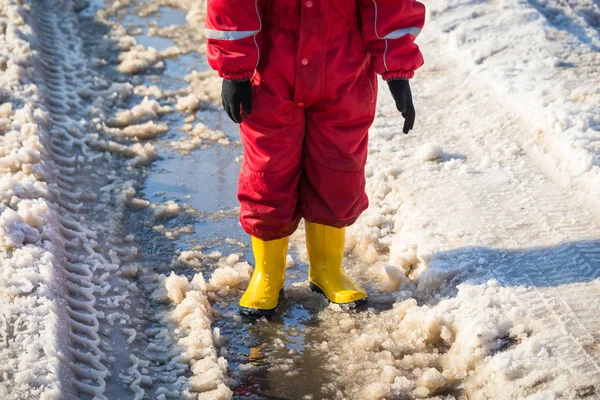 Kid benen in regenlaarsjes staande in de plas van ijs — Stockfoto