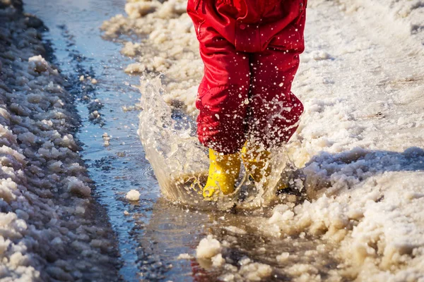 Kid benen in regenlaarsjes springen in de plas van ijs — Stockfoto