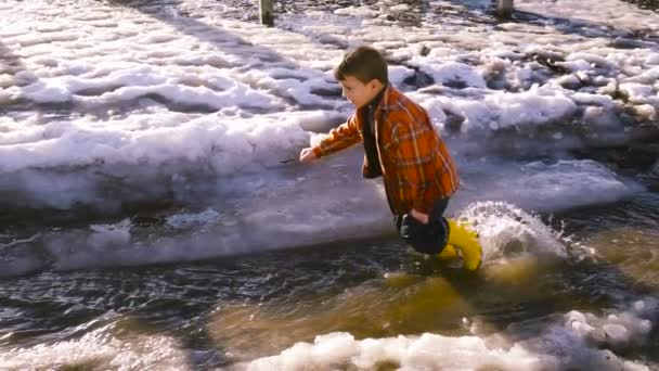 Niño corriendo en el arroyo de primavera con hielo derretido — Vídeos de Stock