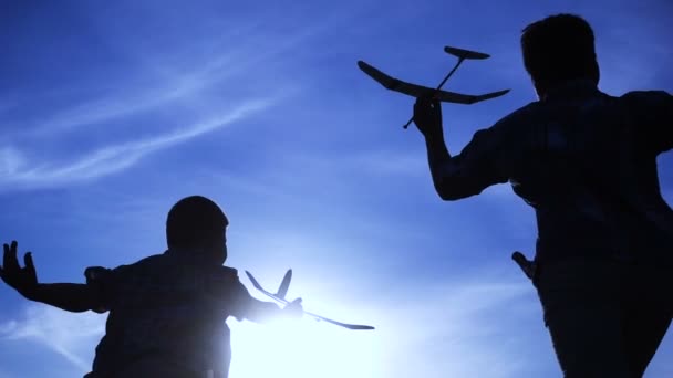 Silhouette zweier Jungen, die bei Sonnenuntergang mit Flugzeugen rennen — Stockvideo