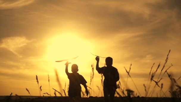Silhueta de dois meninos correndo com aviões ao pôr do sol — Vídeo de Stock