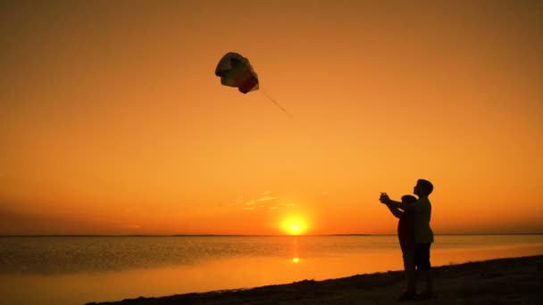 Due bambini che lanciano l'aquilone arcobaleno insieme al tramonto — Video Stock