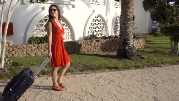 Young girl in red dress traveling on street with suitcase — Stock Video