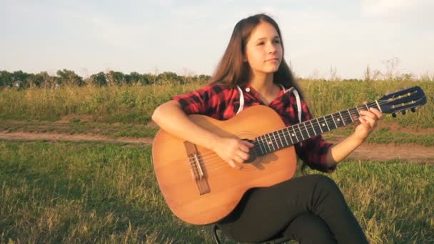 Молодая девушка играет на гитаре на лугу на закате — стоковое видео
