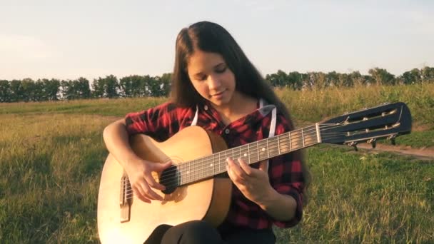 Junges Mädchen spielt Gitarre auf der Wiese bei Sonnenuntergang — Stockvideo