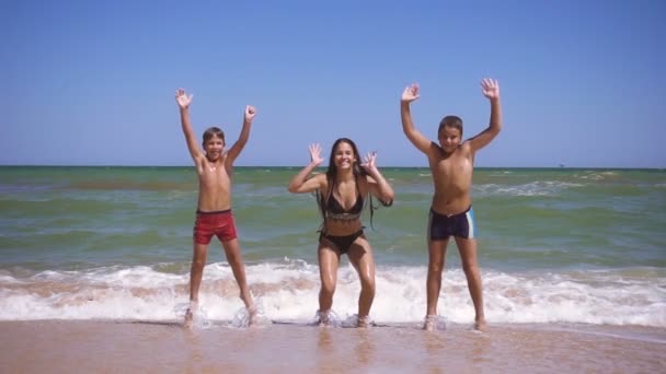 Usmívající se děti skáčou po pláži u příboje — Stock video