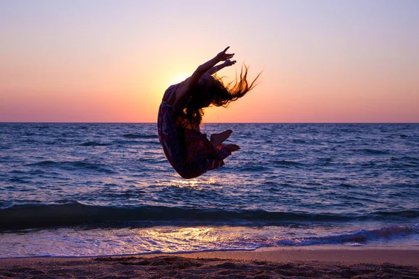 Flicka hoppar på havet kusten vid soluppgången — Stockfoto