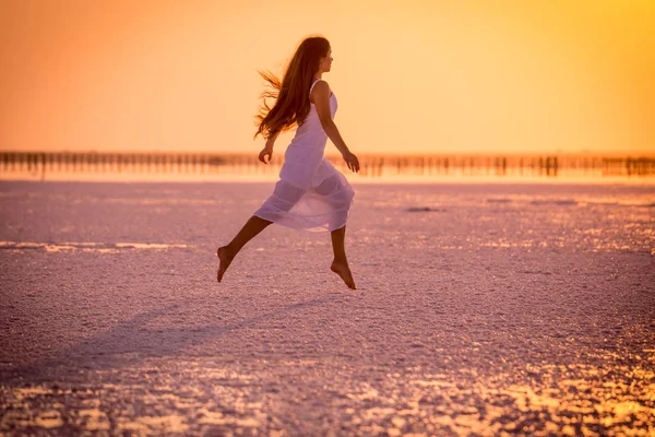 Красива молода дівчина стрибає на солоному озері на заході сонця — стокове фото