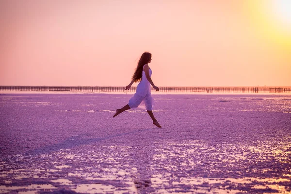Krásná mladá dívka skákající po solném jezeře při západu slunce — Stock fotografie