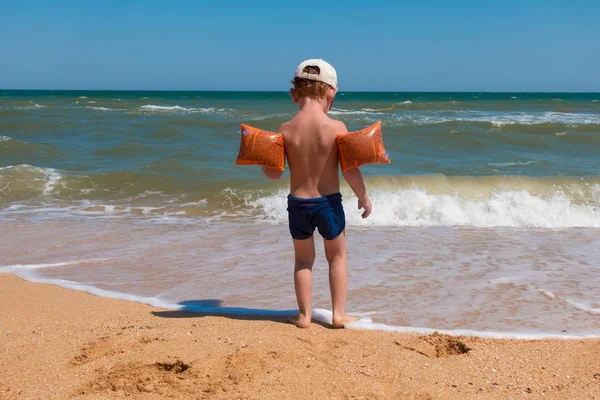 Мальчик, стоящий на берегу моря на серфинге и глядя на воду — стоковое фото