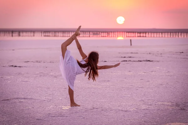 Silhouette di ragazza che fa esercizi sul lago salato al tramonto — Foto Stock