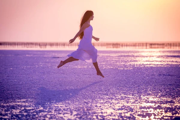 Menina bonita pulando no lago de sal ao pôr do sol — Fotografia de Stock
