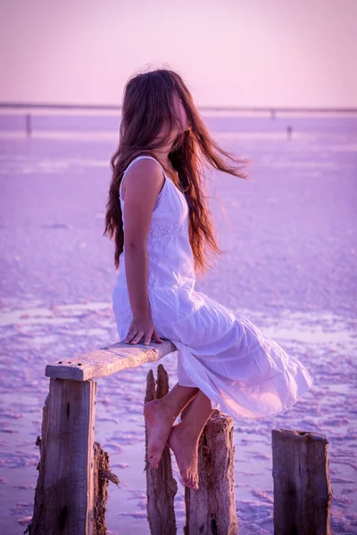 Bella ragazza seduta sulla recinzione sul lago salato — Foto Stock