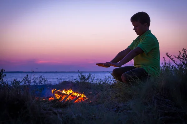 Niño calienta junto a la fogata en la playa al atardecer —  Fotos de Stock