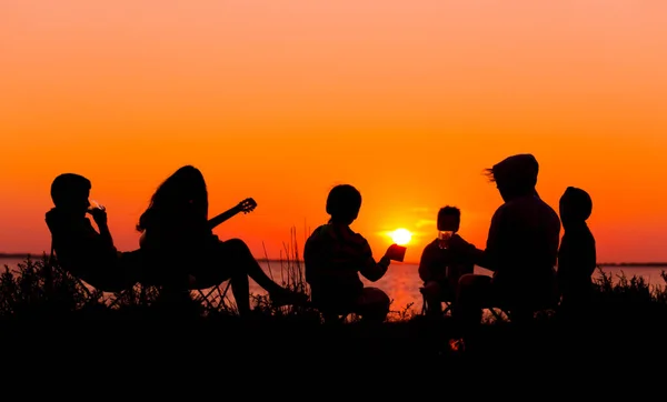 Silhouette de personnes assises sur la plage avec feu de camp au soleil — Photo