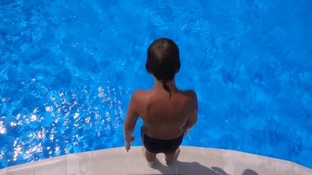 Мальчик прыгает в синий бассейн, замедленная съемка, вид с воздуха — стоковое видео