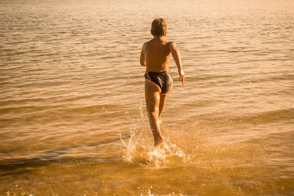 Garçon courant sur l'eau avec des éclaboussures — Photo