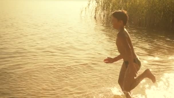 Мальчик бежит по воде с брызгами — стоковое видео