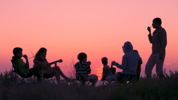 Personas sentadas en la playa con fogata al atardecer — Vídeos de Stock