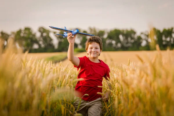小麦畑でおもちゃの飛行機で走る少年 — ストック写真
