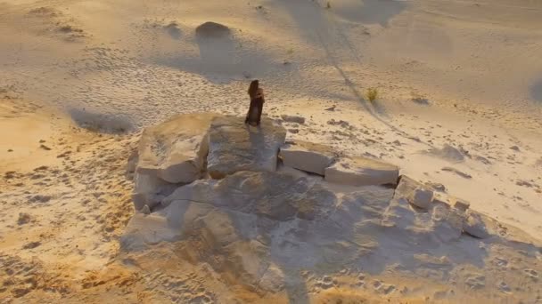 日落时分 穿着黑色衣服的女孩站在岩石前的沙丘上 俯瞰天空 — 图库视频影像