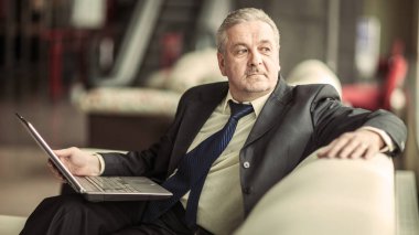 özel bir ofis kanepe üzerinde oturan dizüstü bilgisayar üzerinde çalışan deneyimli iş adamı
