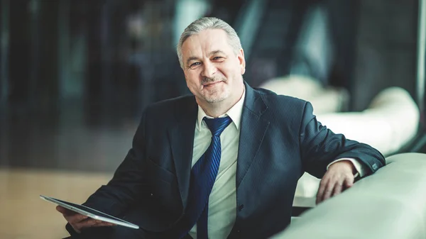 Portrait of businessman with digital tablet sitting in the chair in front of the office. — Stock Photo, Image