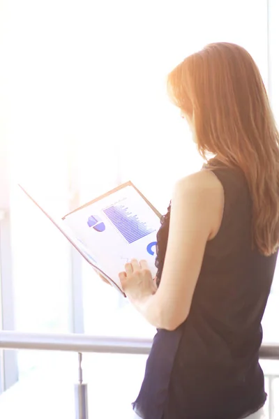 Mujer de negocios moderna con gráficos financieros, mientras que de pie cerca de una gran ventana de oficina — Foto de Stock