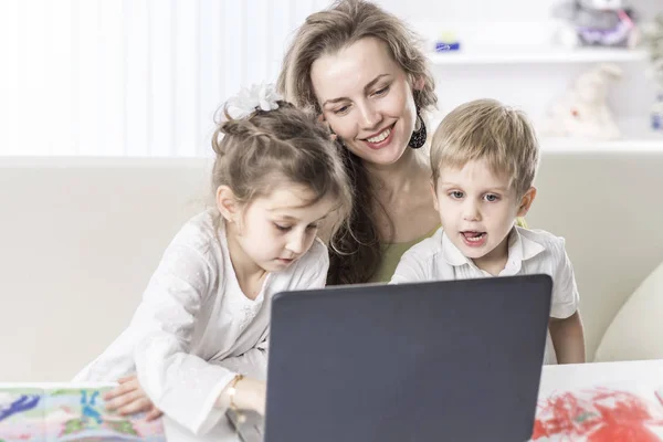 Молодая мама - деловая женщина, работающая на ноутбуке и разговаривающая на смартфоне рядом со своими детьми — стоковое фото