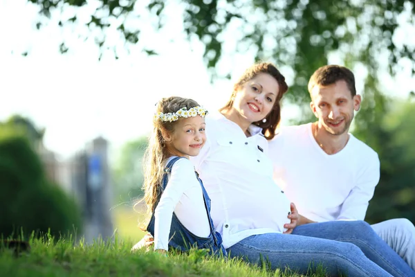 Padres expectantes y su hijita sentada en la hierba — Foto de Stock