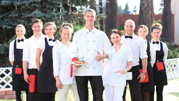 Grande gruppo di cuochi e cameriere stare in fila dietro lo chef — Foto Stock