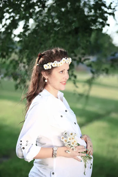 Happy těhotná žena v věnce a kytice divokých květin o — Stock fotografie